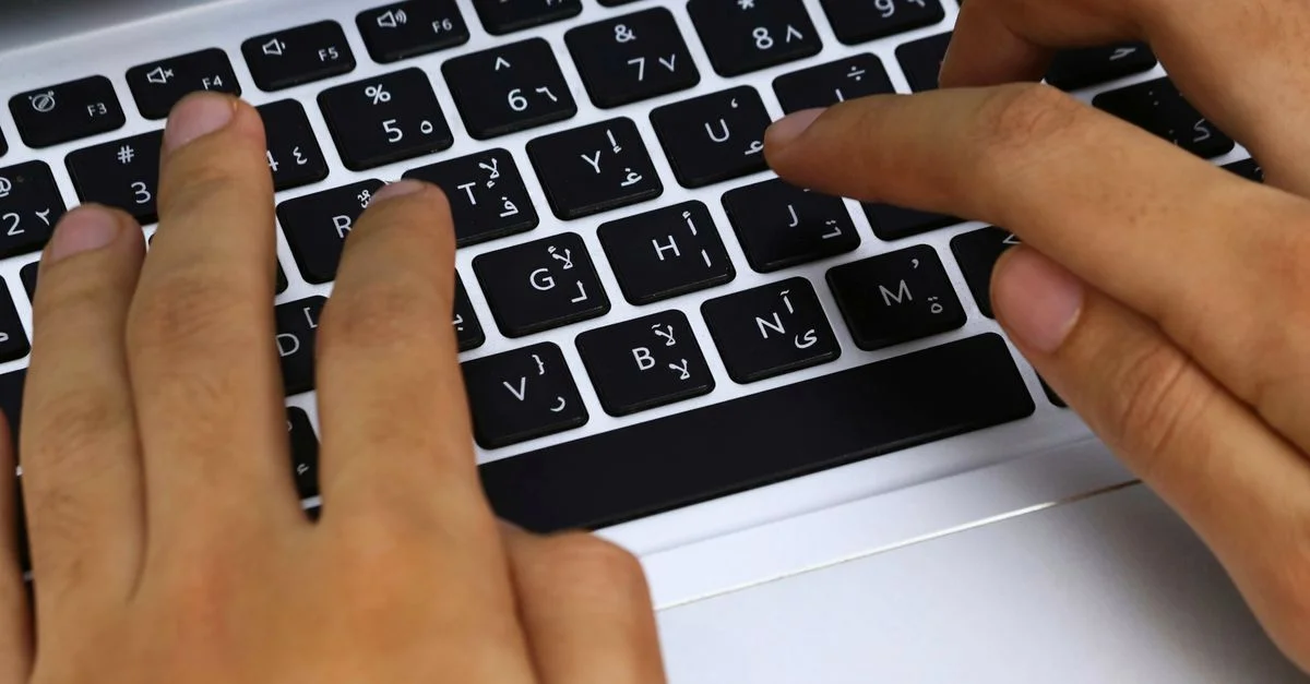 Gros plan de mains tapant sur un clavier d'ordinateur portable de disposition arabe, mettant en valeur la technologie moderne en cours d'utilisation.