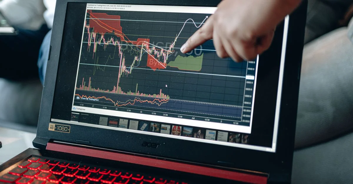 Une personne pointe sur un graphique sur un ordinateur portable, analysant les tendances boursières pour des insights d'investissement.