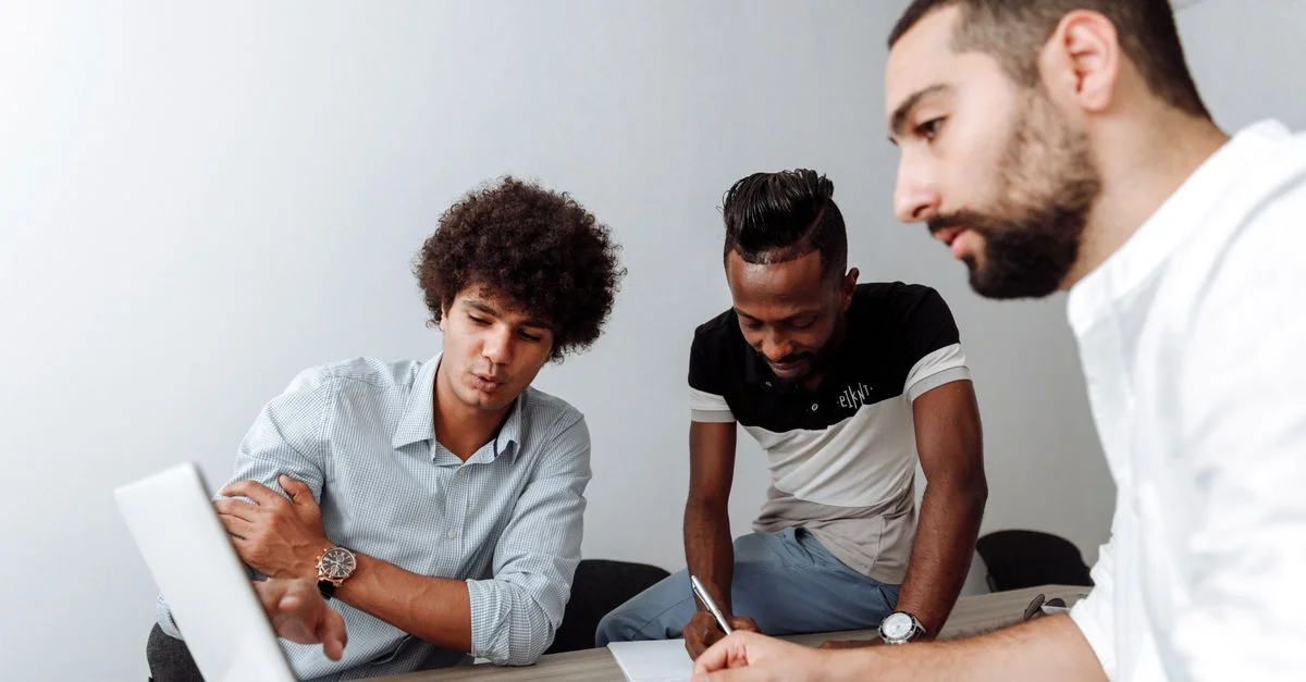 Groupe diversifié de jeunes hommes collaborant dans une salle de réunion de bureau avec un ordinateur portable.