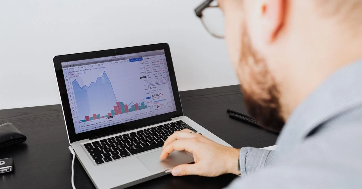 Homme travaillant sur un ordinateur portable, analysant des données commerciales et des graphiques financiers à l'intérieur.