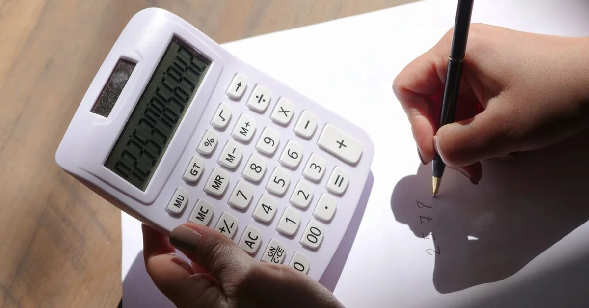 Gros plan sur des mains tenant une calculatrice et écrivant sur du papier, représentant le calcul et l'analyse.